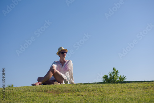 Woman lying and reading her favorite book on a meadow covered with fresh green grass on a sunny summer or spring day.