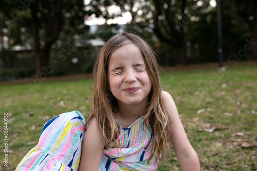 Girl pulling silly face with eyes closed sitting outside on grass