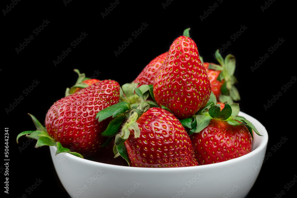 Ripe red strawberries with green tails in a white plate on a black background. Sweet dessert of fresh berries on the table. Ripe red strawberries with green tails in a white plate on a black background. Sweet dessert of fresh berries on the table.