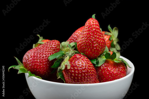 Ripe red strawberries with green tails in a white plate on a black background. Sweet dessert of fresh berries on the table.