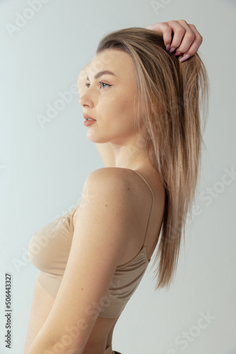 Side view portrait of young stunning blonde girl posing in beige underwear isolated over grey studio background. Natural beauty