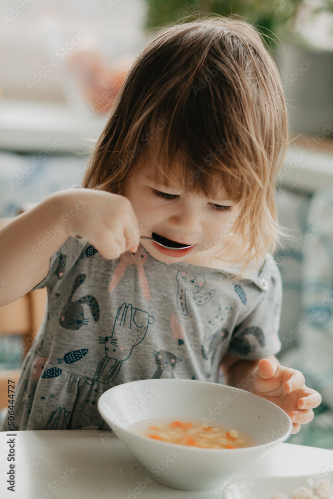 a little girl is sitting at the kitchen table eating soup a little girl is sitting at the kitchen table eating soup
