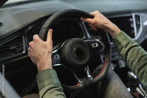 Closeup view of young man holding steering wheel of modern luxury car, going on test drive at modern auto dealership © Prostock-studio