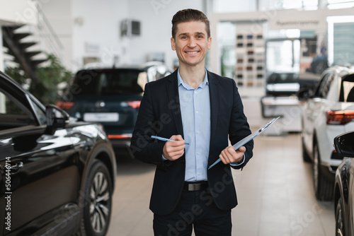 Portrait of positive young auto insurance agent posing in automobile dealership center © Prostock-studio