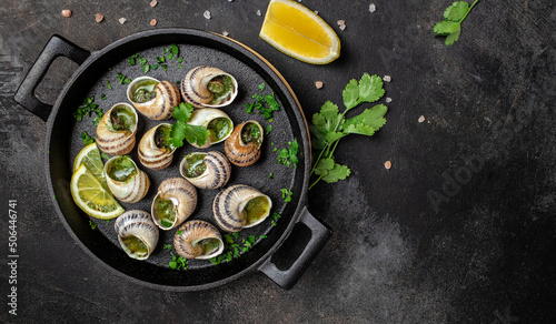 Fototapeta Naklejka Na Ścianę i Meble -  Delicious cooked sea escargo snails with herbs, butter, garlic on metal plate on a dark background. gourmet food. Restaurant menu, Traditional French cuisine