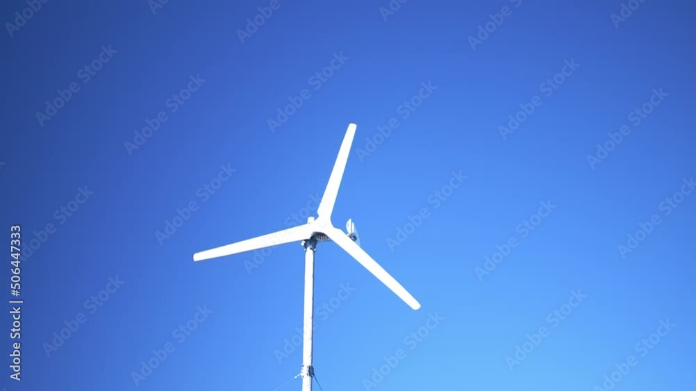 White wind turbine spinning against blue sky, reveal shot from fence pole White wind turbine spinning against blue sky, reveal shot from fence pole