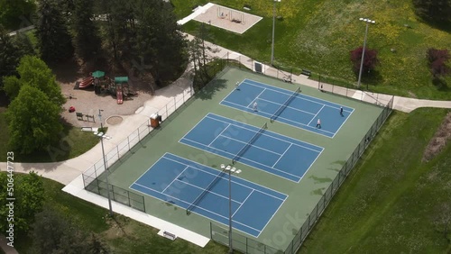 An aerial shot of hard tennis courts, where players are playing doubles. Courts are located in a a park photo