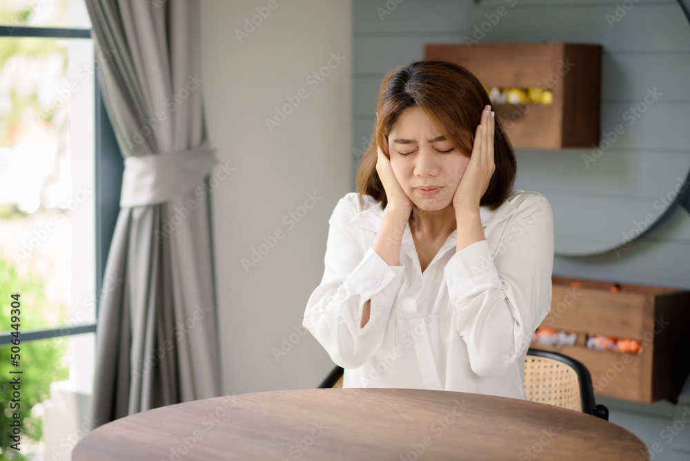 An Asian woman places her hands near her head while suffering from a headache. An Asian woman places her hands near her head while suffering from a headache.