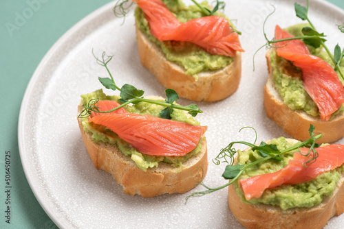 Open sandwich with salted salmon, avocado guacamole and microgreens on a plate. Green pastel background. The concept of healthy and diet food. Side view, selective focus.