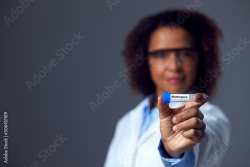 Studio Portrait of Female Lab Research Worker Wearing PPE Holding Test Tube Labelled Monkeypox