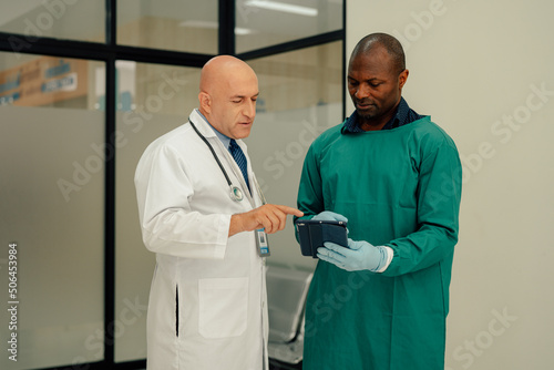 Male Surgeon and Doctor Consult Using Digital Tablet Computer while Talking about Patient's Health.