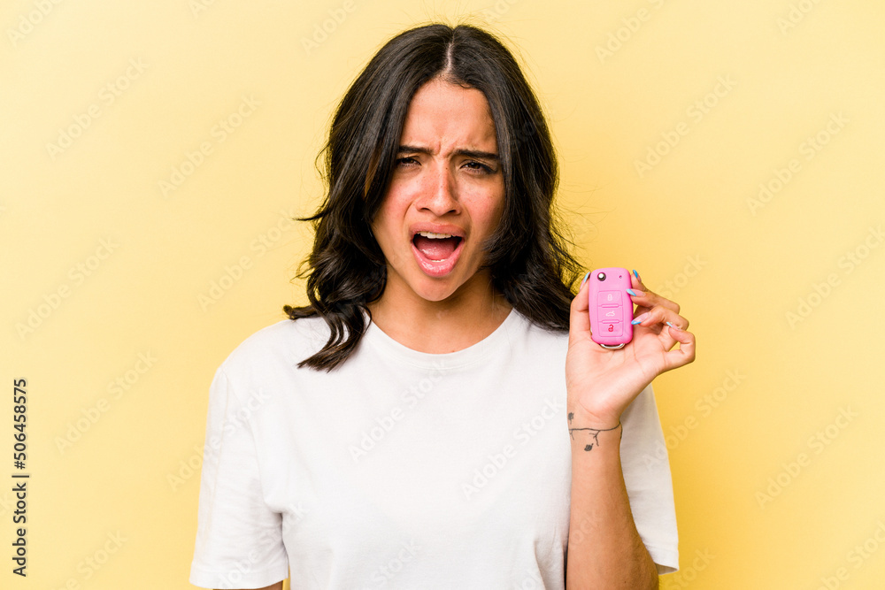 Young hispanic woman holding a keys car isolated on pink background screaming very angry and aggressive. Young hispanic woman holding a keys car isolated on pink background screaming very angry and aggressive.