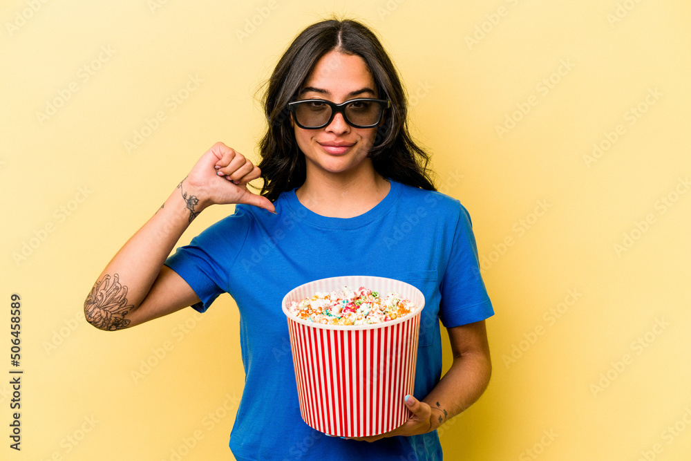 Young hispanic woman holding popcorn isolated on yellow background feels proud and self confident, example to follow. Young hispanic woman holding popcorn isolated on yellow background feels proud and self confident, example to follow.