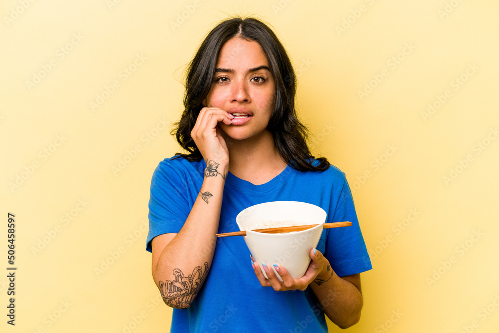 Young hispanic woman eating ramen isolated on blue background biting fingernails, nervous and very anxious. Young hispanic woman eating ramen isolated on blue background biting fingernails, nervous and very anxious.