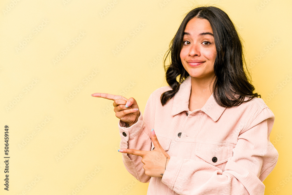 Young hispanic woman isolated on yellow background shocked pointing with index fingers to a copy space.