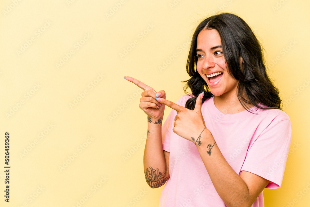 Young hispanic woman isolated on yellow background points with thumb finger away, laughing and carefree. Young hispanic woman isolated on yellow background points with thumb finger away, laughing and carefree.