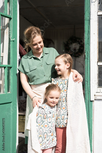 happy family mother with little kids daughters helper girls have fun in suburb countryside life on laundry day. candid mom hug and cover children with plaid and doing chores on porch of country house