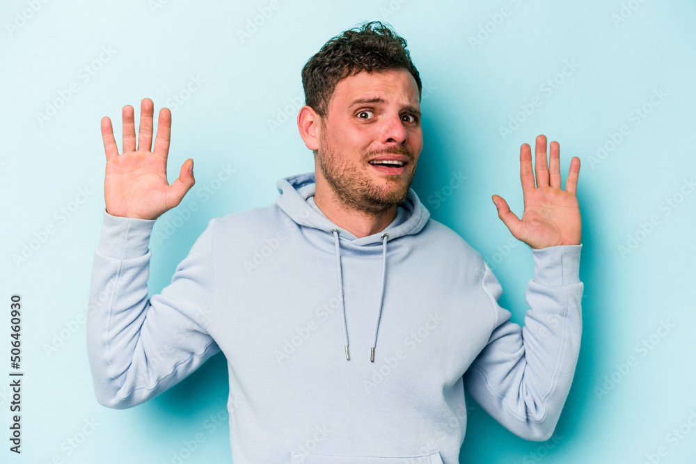 Young caucasian man isolated on blue background being shocked due to an imminent danger Young caucasian man isolated on blue background being shocked due to an imminent danger