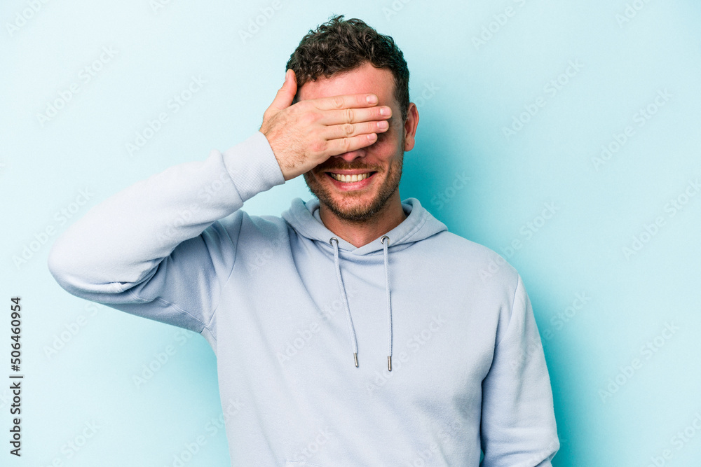 Young caucasian man isolated on blue background covers eyes with hands, smiles broadly waiting for a surprise. Young caucasian man isolated on blue background covers eyes with hands, smiles broadly waiting for a surprise.