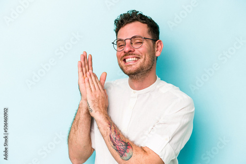 Obraz na plátně Young caucasian man isolated on blue background feeling energetic and comfortable, rubbing hands confident