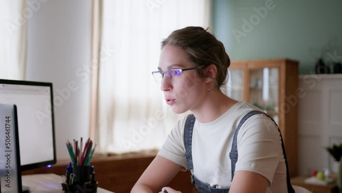 young woman remote works in home office, sitting at table with laptop. has video call using web cam, argues, blows up and disputes. Looks angry and dissatisfied. girl swears using online network