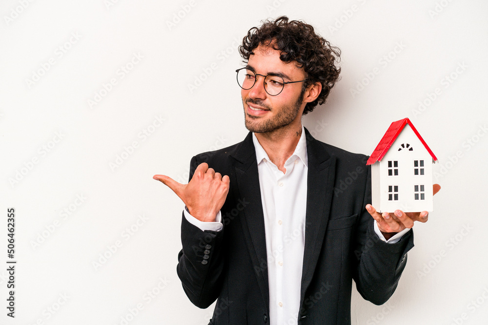 Young caucasian business man holding a toy house isolated on white background points with thumb finger away, laughing and carefree. Young caucasian business man holding a toy house isolated on white background points with thumb finger away, laughing and carefree.