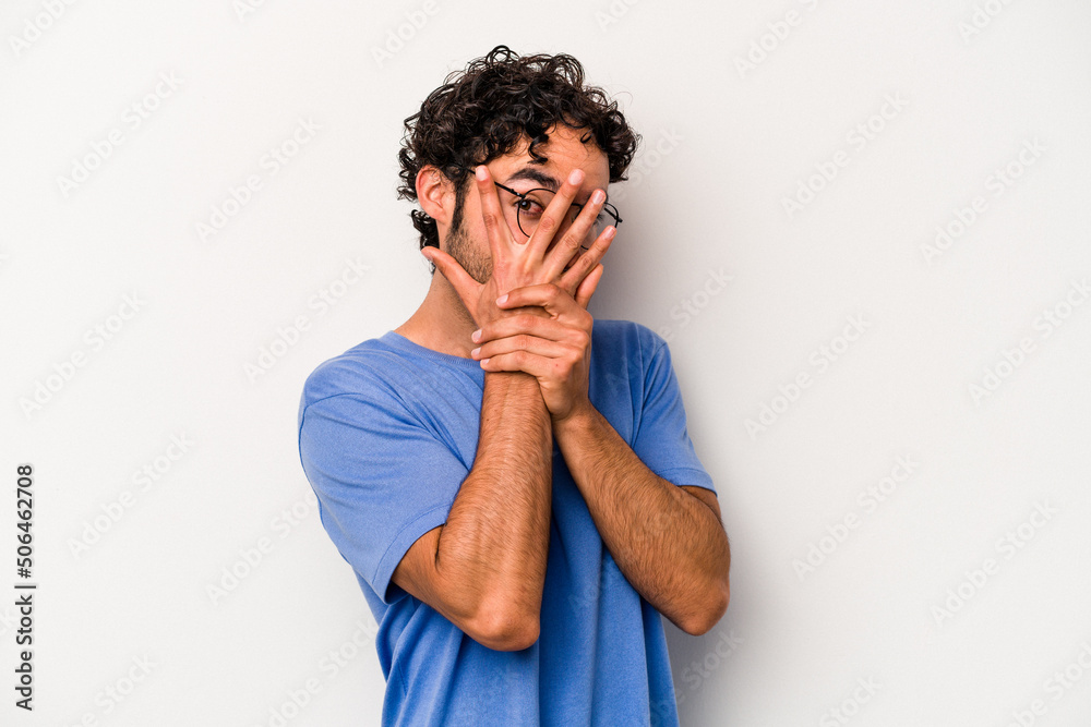 Young caucasian man isolated on white background blink through fingers frightened and nervous.