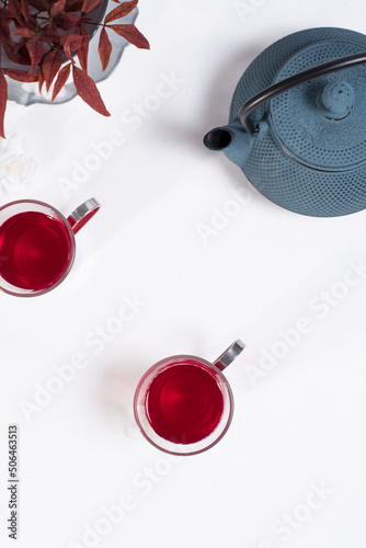 Dos tazas transparentes de té de bayas con tetera de hierro azul sobre una mesa blanca. Vista superior