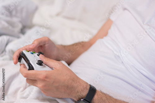 Young man playing video games at home. Close-up of a man's hands playing games console on a white controller in a white bed. Concept: free time hobby rest at home 