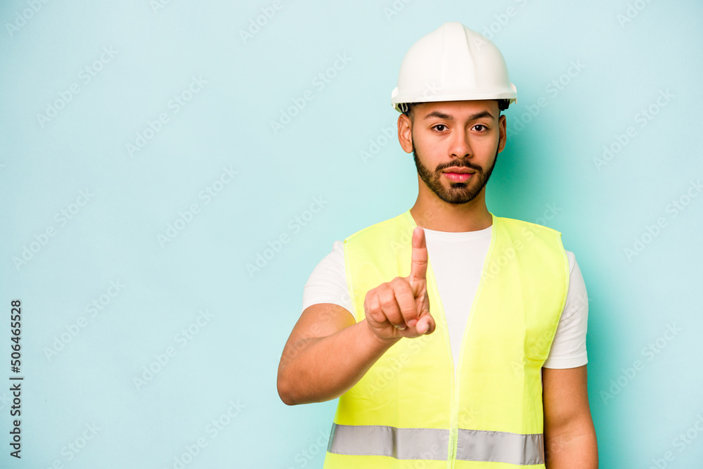 Young laborer hispanic man isolated on blue background showing number one with finger. Young laborer hispanic man isolated on blue background showing number one with finger.