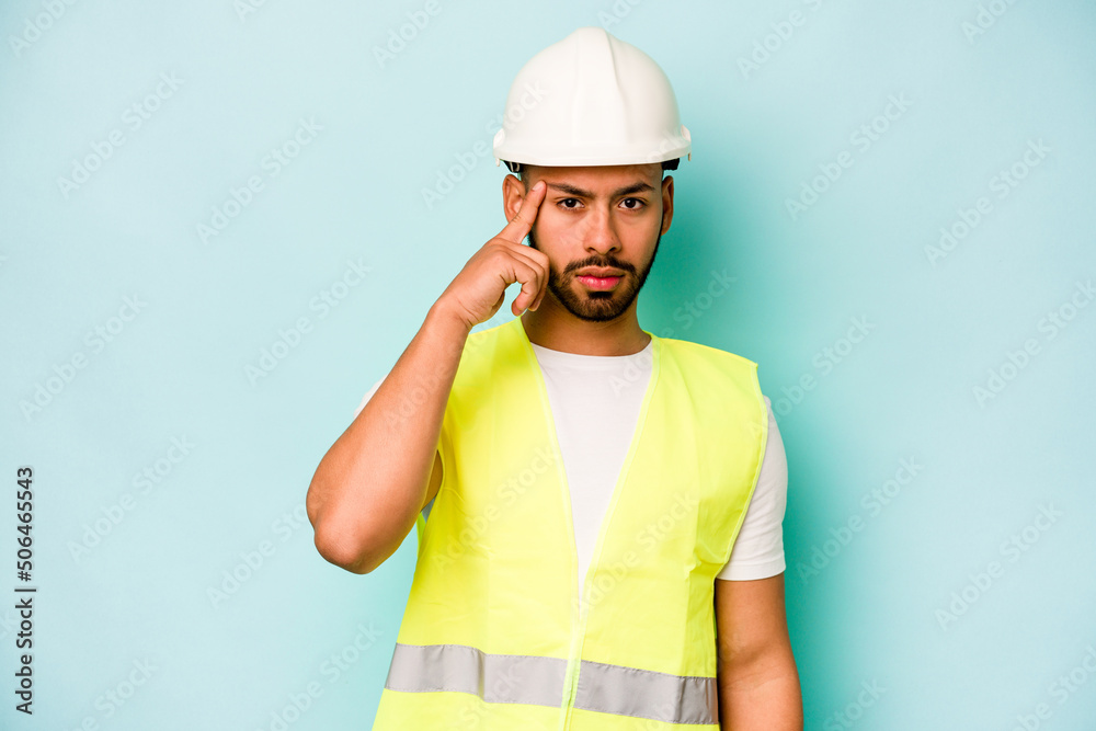 Young laborer hispanic man isolated on blue background pointing temple with finger, thinking, focused on a task.