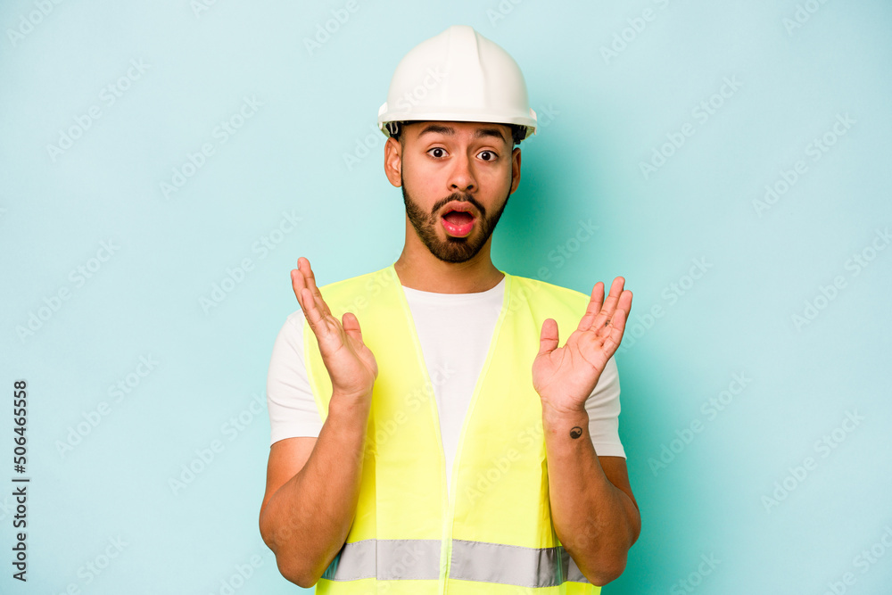 Young laborer hispanic man isolated on blue background surprised and shocked. Young laborer hispanic man isolated on blue background surprised and shocked.