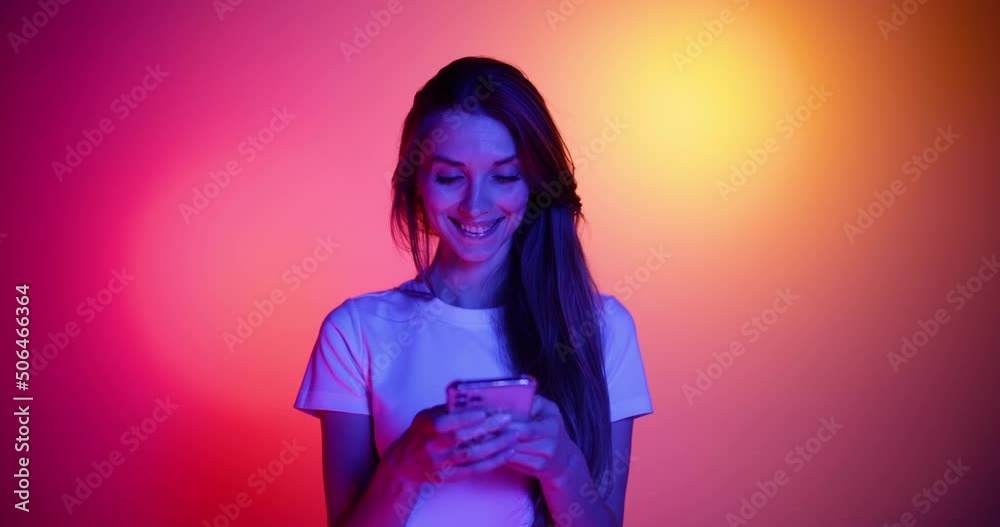 Excited young girl in eyewear using phone, watching funny video isolated on red-yellow background in neon light, filter. 4K. Emotions, ads, culture, youth concept Excited young girl in eyewear using phone, watching funny video isolated on red-yellow background in neon light, filter. 4K. Emotions, ads, culture, youth concept