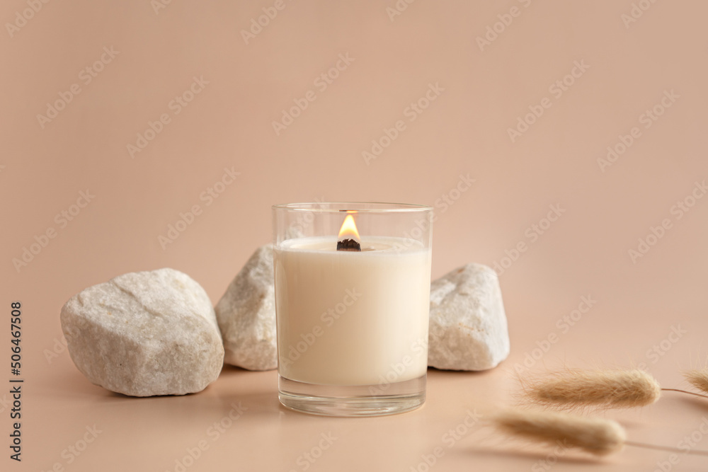Vanilla burning candle on beige background. Warm aesthetic composition with stones and dry flowers. Home comfort, spa, relax and wellness concept. Interior decoration - obrazy, fototapety, plakaty 