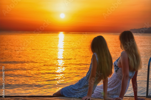 Rear view of mom and daughter by the sea meeting morning sunrise. Summer holiday, communication and travel concept. Horizontal image. © zwiebackesser
