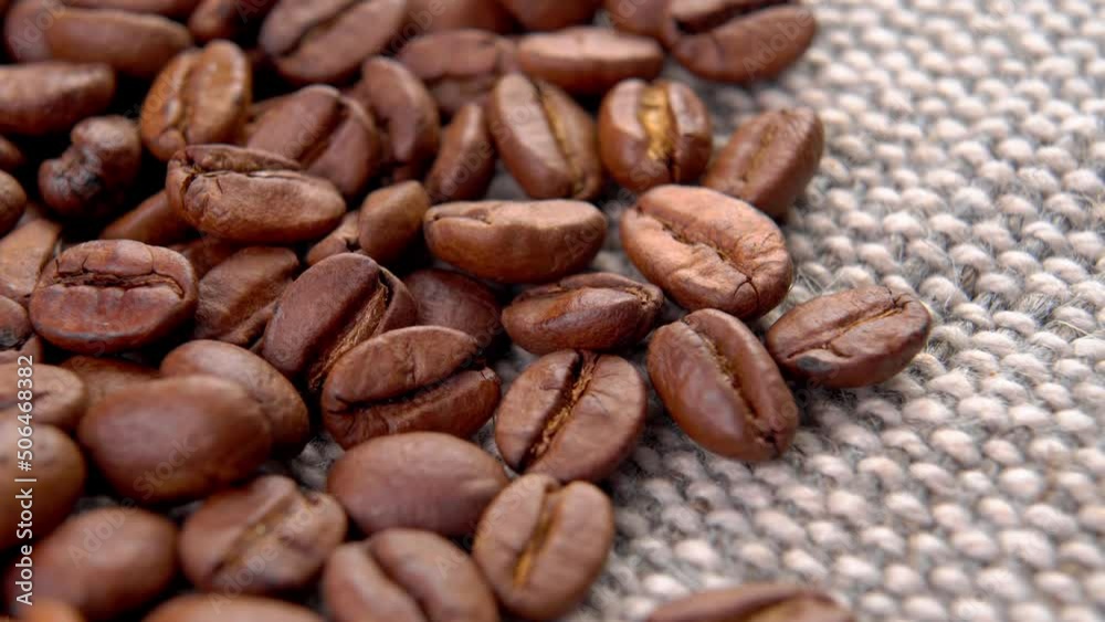 Roasted coffee beans on rough rustic jute cloth. Brown Arabica aromatic drink ingredient. Macro. Rotation