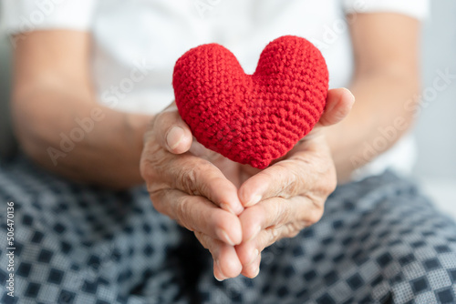 Senior woman holding red yarn heart shape concept of healthcare for elderly heart attack and surgery. Healthy lifestyle or hope for grandparent.