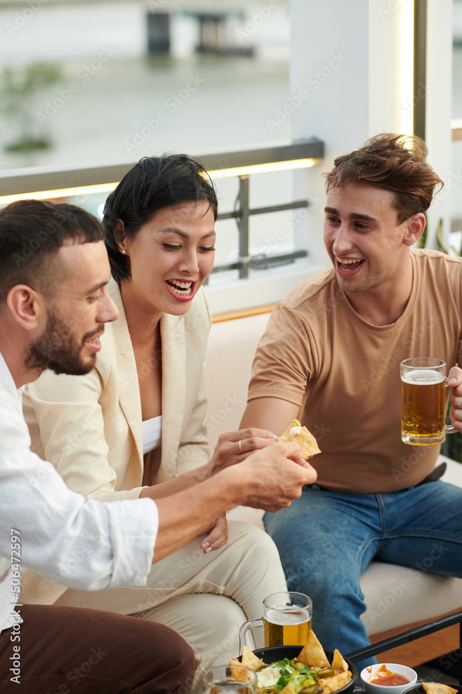 Joyful group of friends having tortilla chips with hot sauce and beer in bar Joyful group of friends having tortilla chips with hot sauce and beer in bar