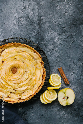 An beautiful apple pie with a lemon swirl and cinnamon stick. The pie is on a black rack and background.