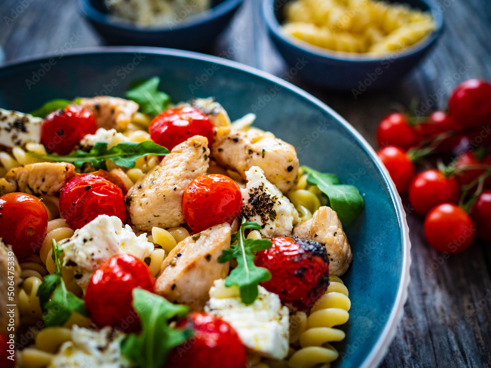 Roasted chicken nuggets, cherry tomatoes, feta cheese and fusilli served on wooden table
Roasted chicken nuggets, cherry tomatoes, feta cheese and fusilli served on wooden table