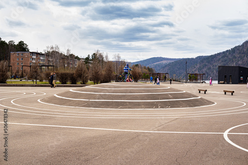 Skate area in the city park, playground for sport activities, a kid riding a bike, mountains in the background