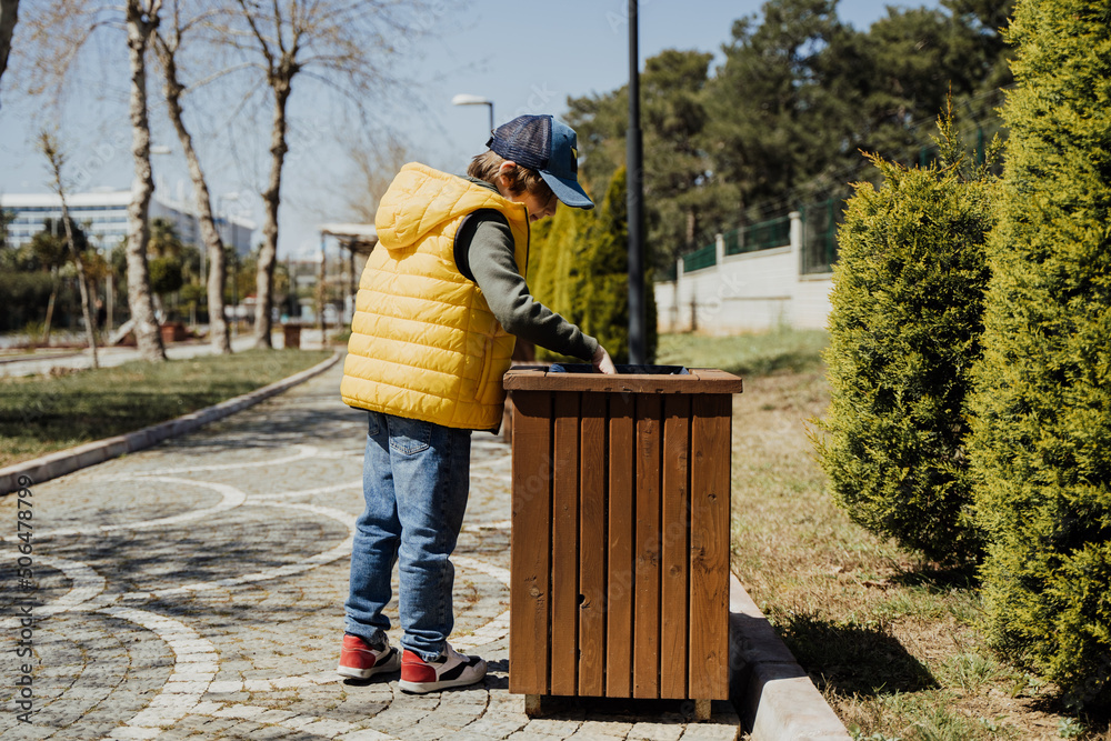 Schoolboy kid throwing the trash into dumpster. Boy using recycling bin