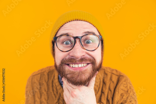 It's time to smile. Positive European lad showing his teeth in a big smile and intensively staring at camera white touching his beard over yellow background. High quality photo