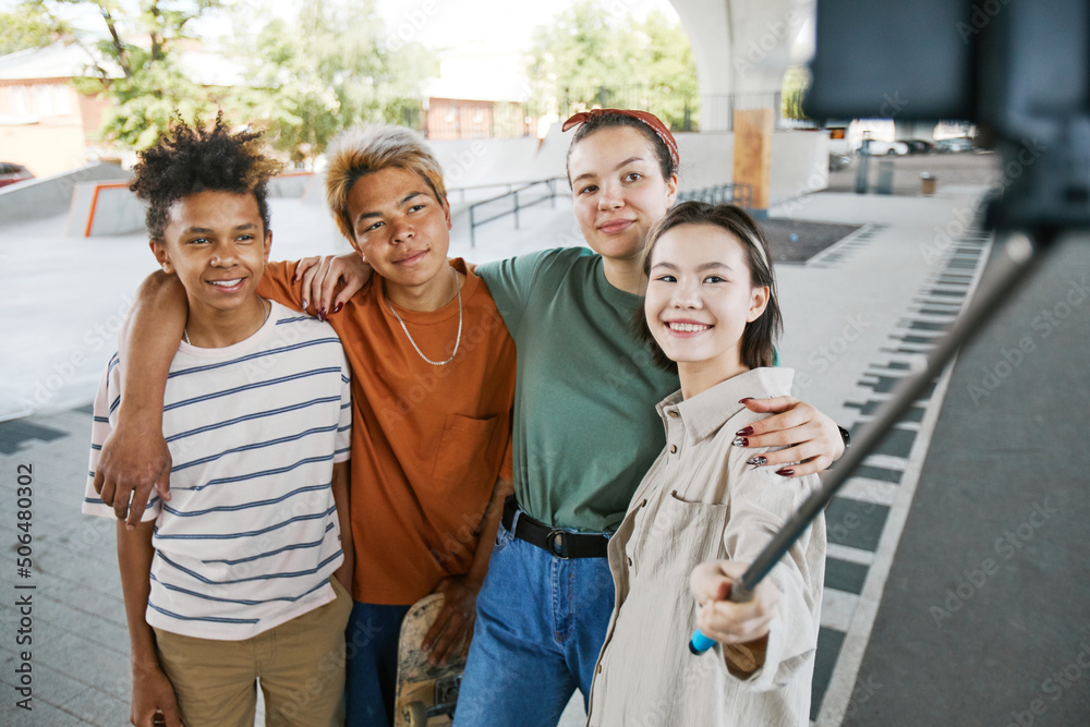 Obraz premium Diverse group of teens taking selfie photo outdoors in urban area using selfie stick