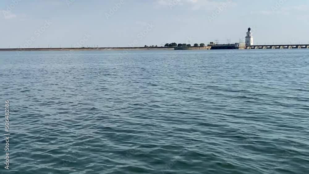 View from the water on coast of Tsimlyansk reservoir. In distance there is a steep coast, a rotunda and platinum against background of sky and sea waves. View from the water on coast of Tsimlyansk reservoir. In distance there is a steep coast, a rotunda and platinum against background of sky and sea waves.