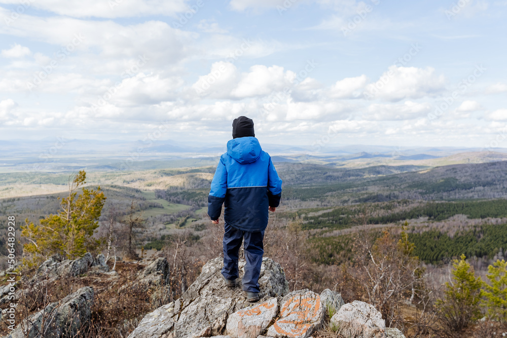 The view from behind of a child standing high in the mountains, the boy traveling through the stones, tourism in the children's scout camp, looking at nature, beautiful landscape.