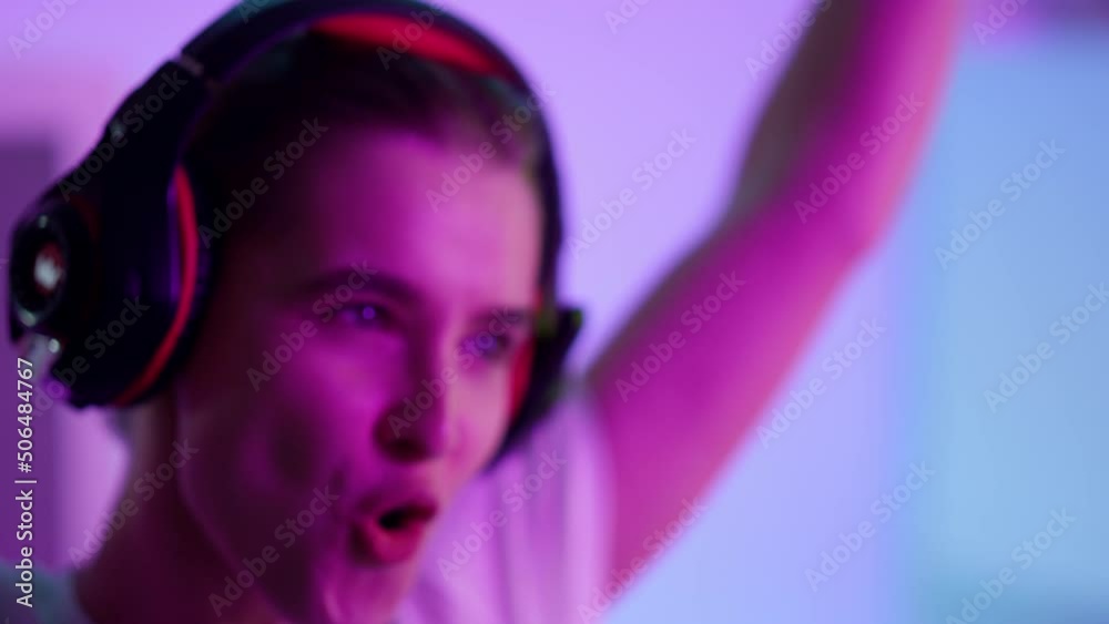 Happy woman celebrating victory in neon room closeup. Smiling girl take headset