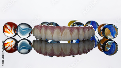 creative photo of a dental prosthesis with a beautiful gum and glass balls with patterns on a white background with reflection