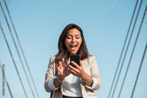 Принти на полотні Portrait of a young latina excitedly looking at her cell phone, smart phone on t