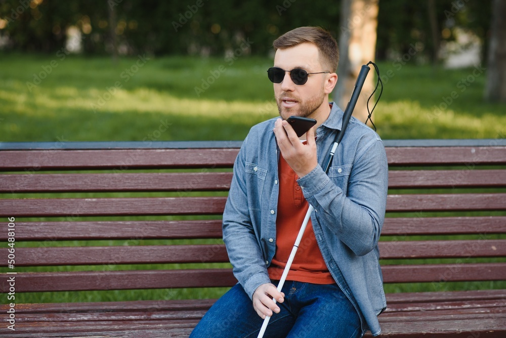 Fototapeta premium Young blinded man using phone and sending voice message